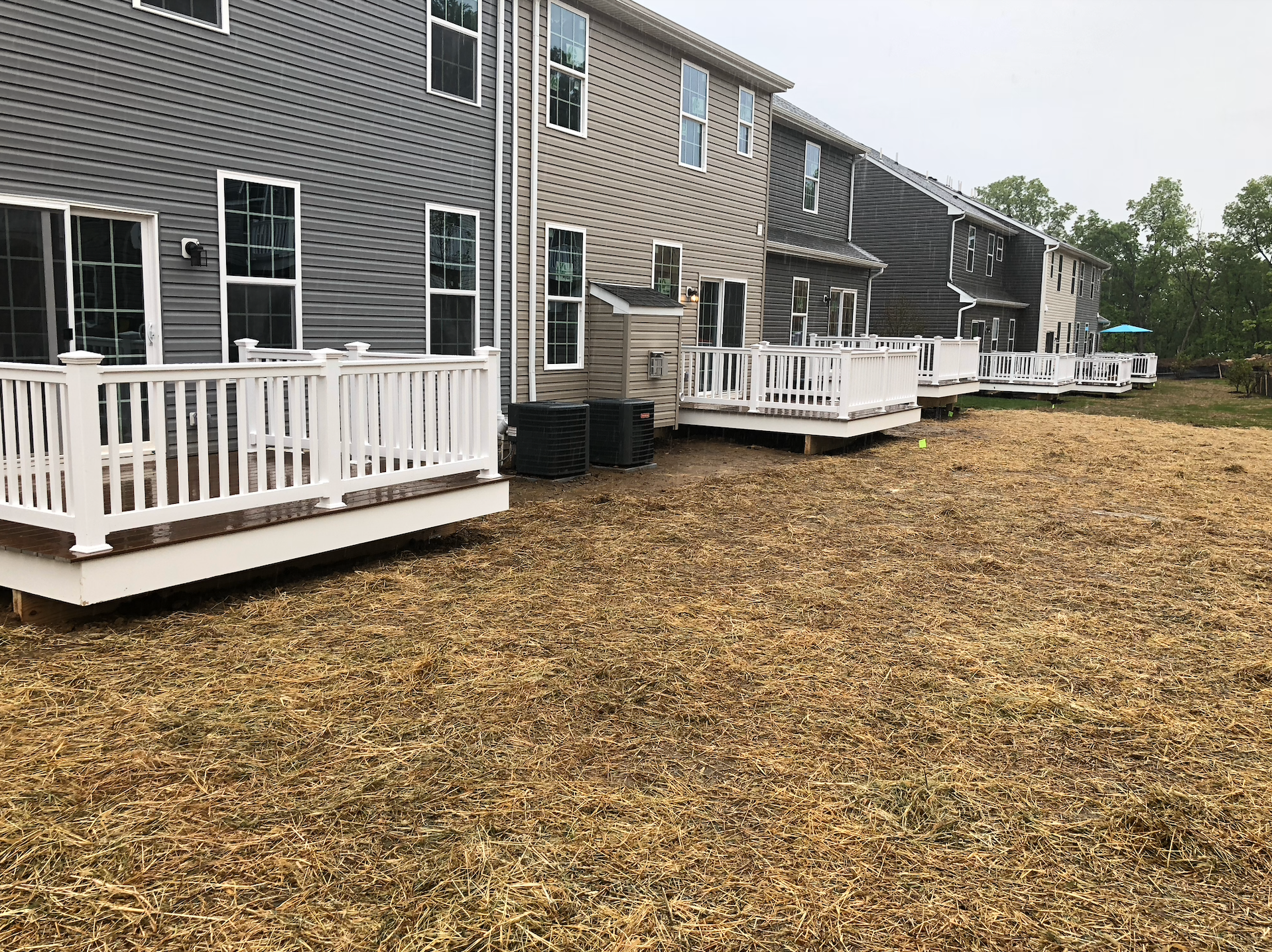Row of townhomes with white decks beside a ground covered in fallen leaves under overcast skies