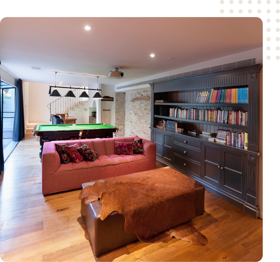 Modern living room with pool table, pink sofa, ottoman, and large bookshelf wall