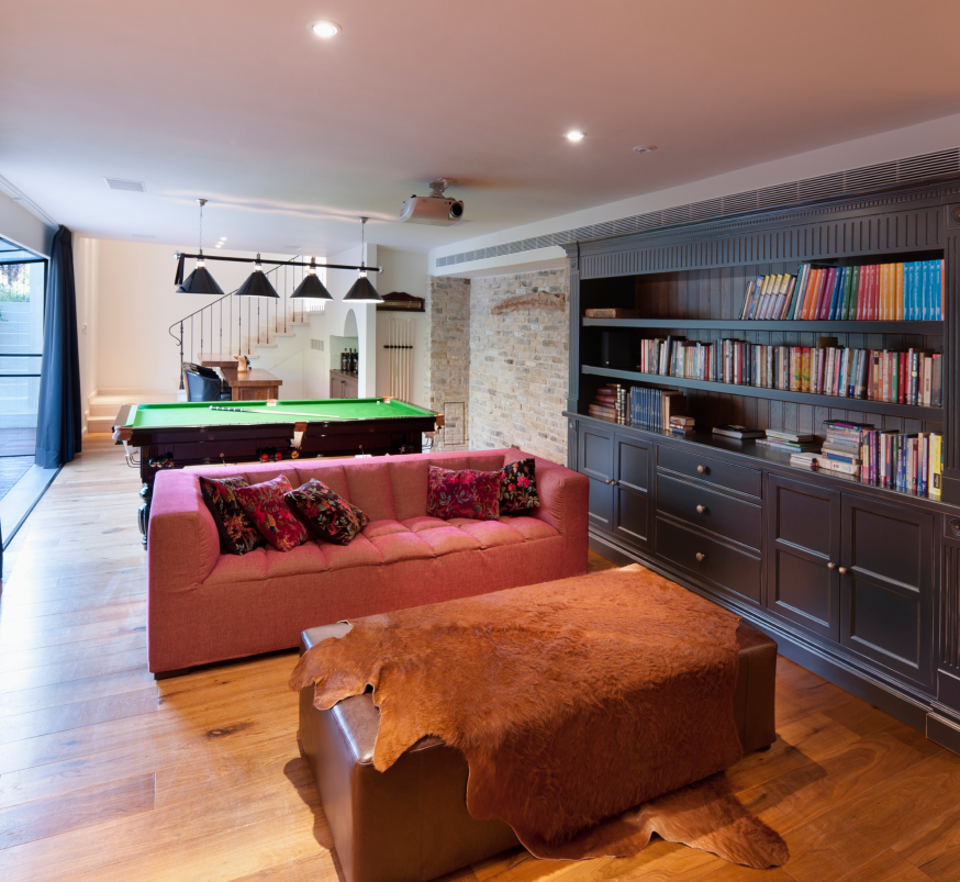 Cozy game room with a pool table, red sofa, leather ottoman, and dark bookcase along the wall