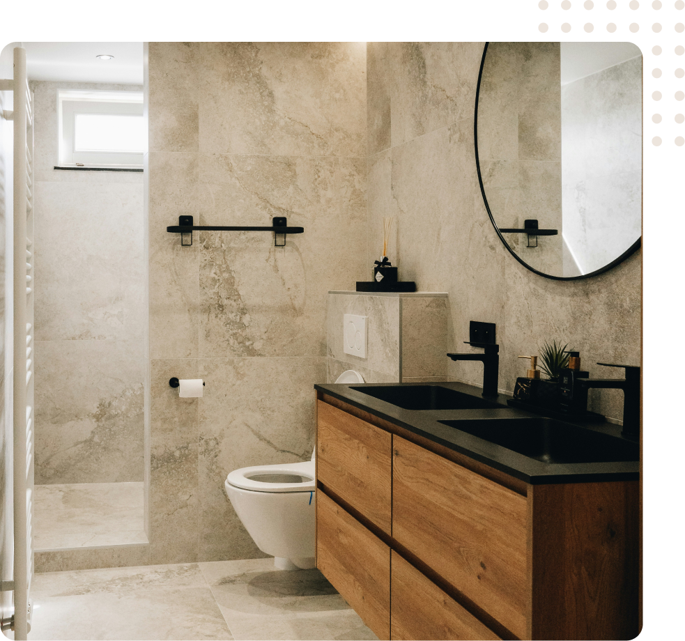 Modern bathroom with wood vanity, black sink, round mirror, and walk-in shower on stone walls