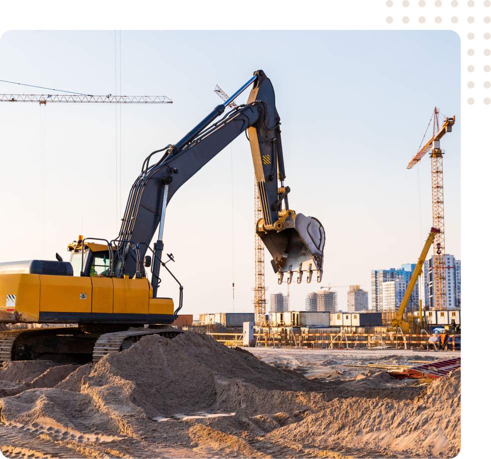 Yellow excavator lifting gravel at a construction site with cranes and buildings in the background