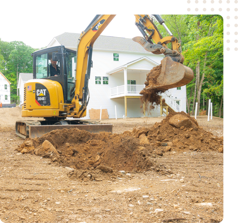 Two excavators digging dirt in a yard in front of a white house