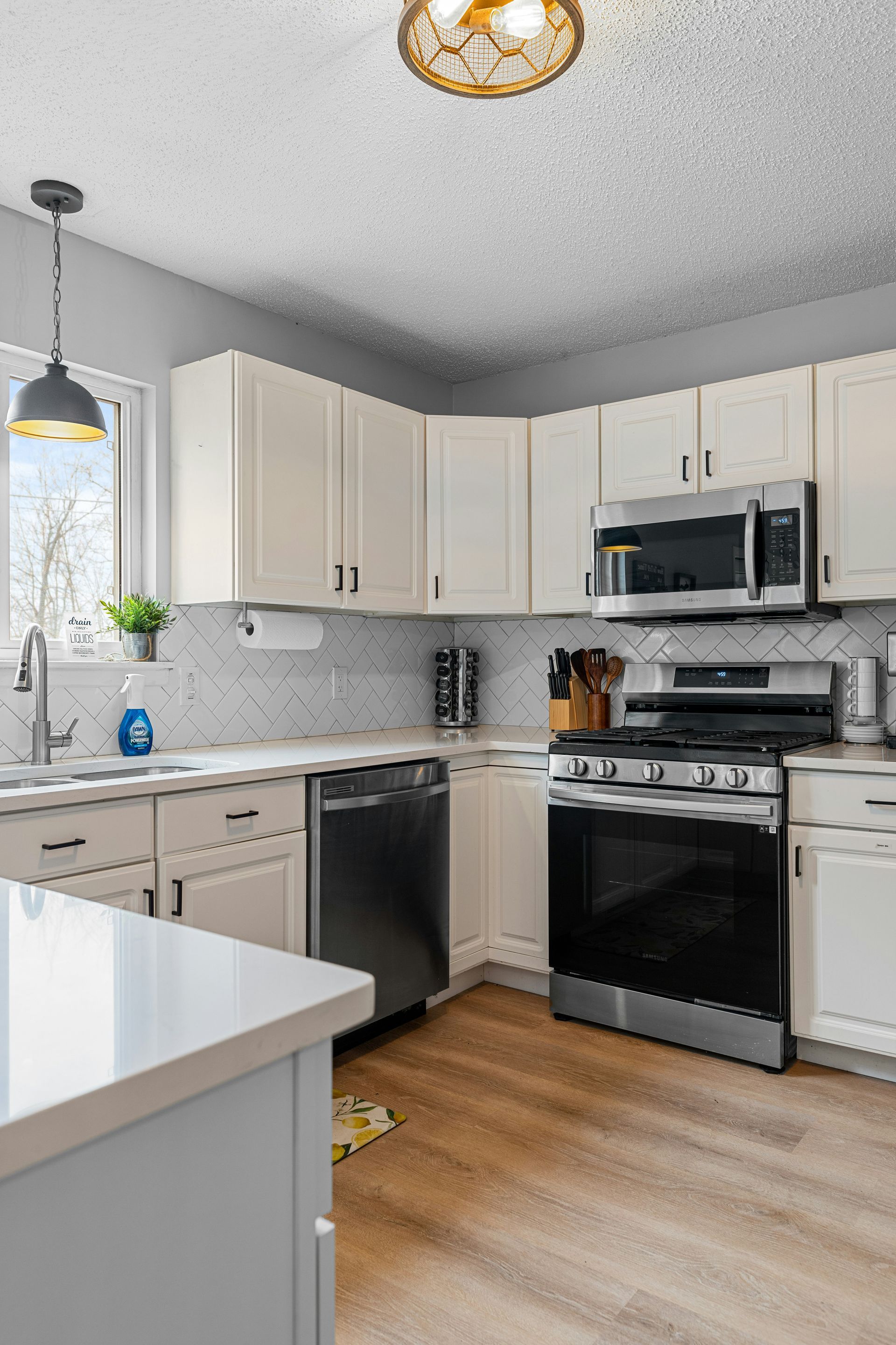Bright modern kitchen with white cabinets, stainless appliances, wood floor, and a pendant light over the island.