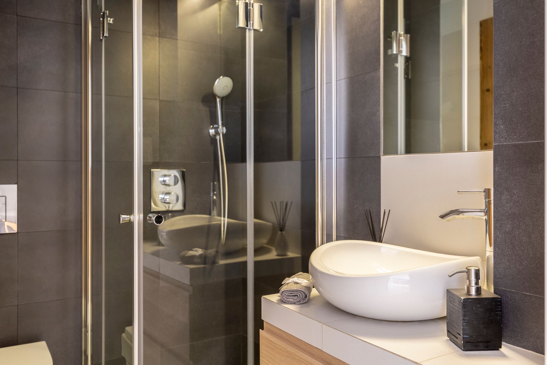 Modern bathroom with glass shower, sink, mirror, and gray tile walls