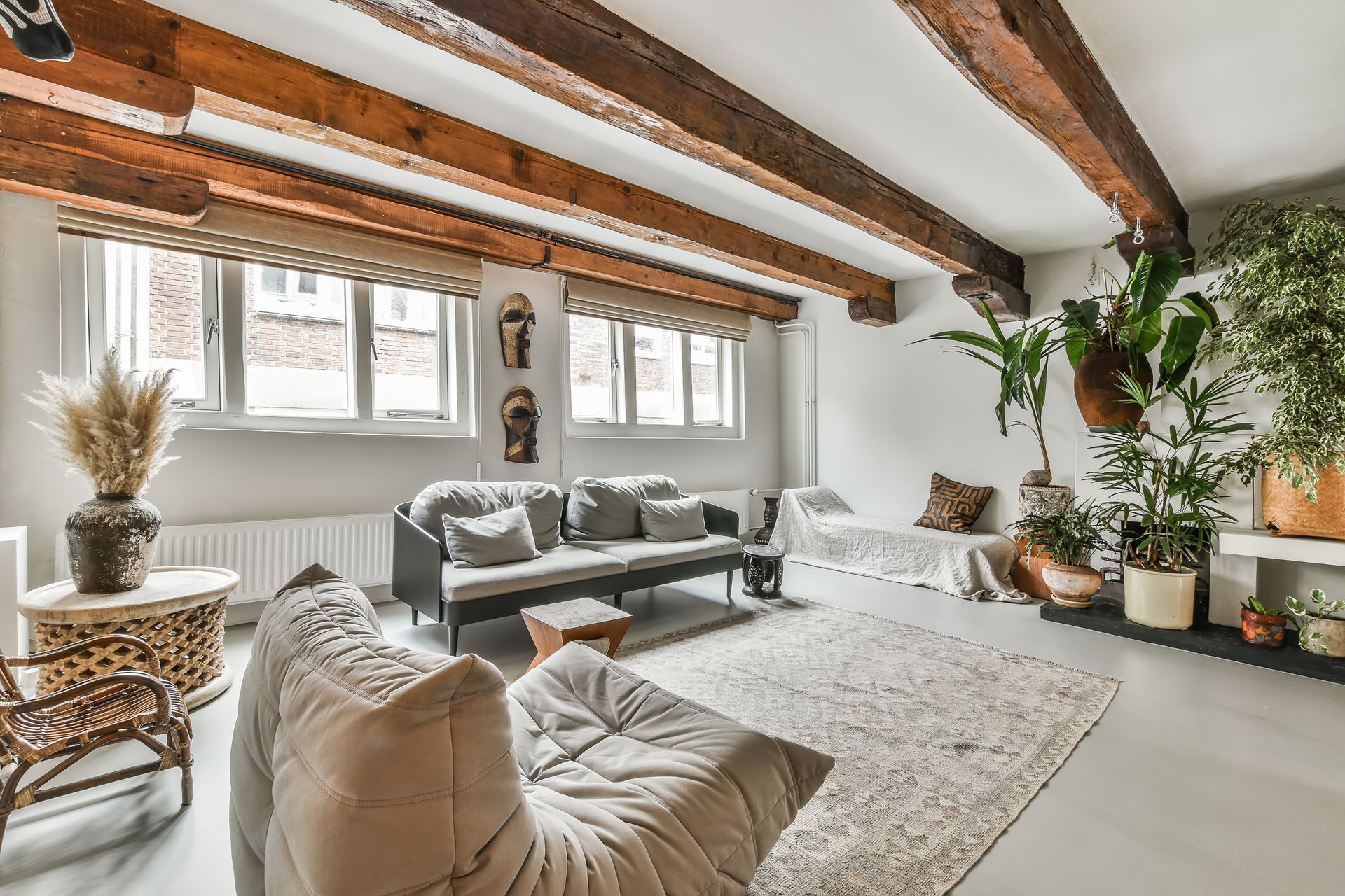 Bright living room with exposed wood beams, gray sofa, armchair, plants, and a large shag rug