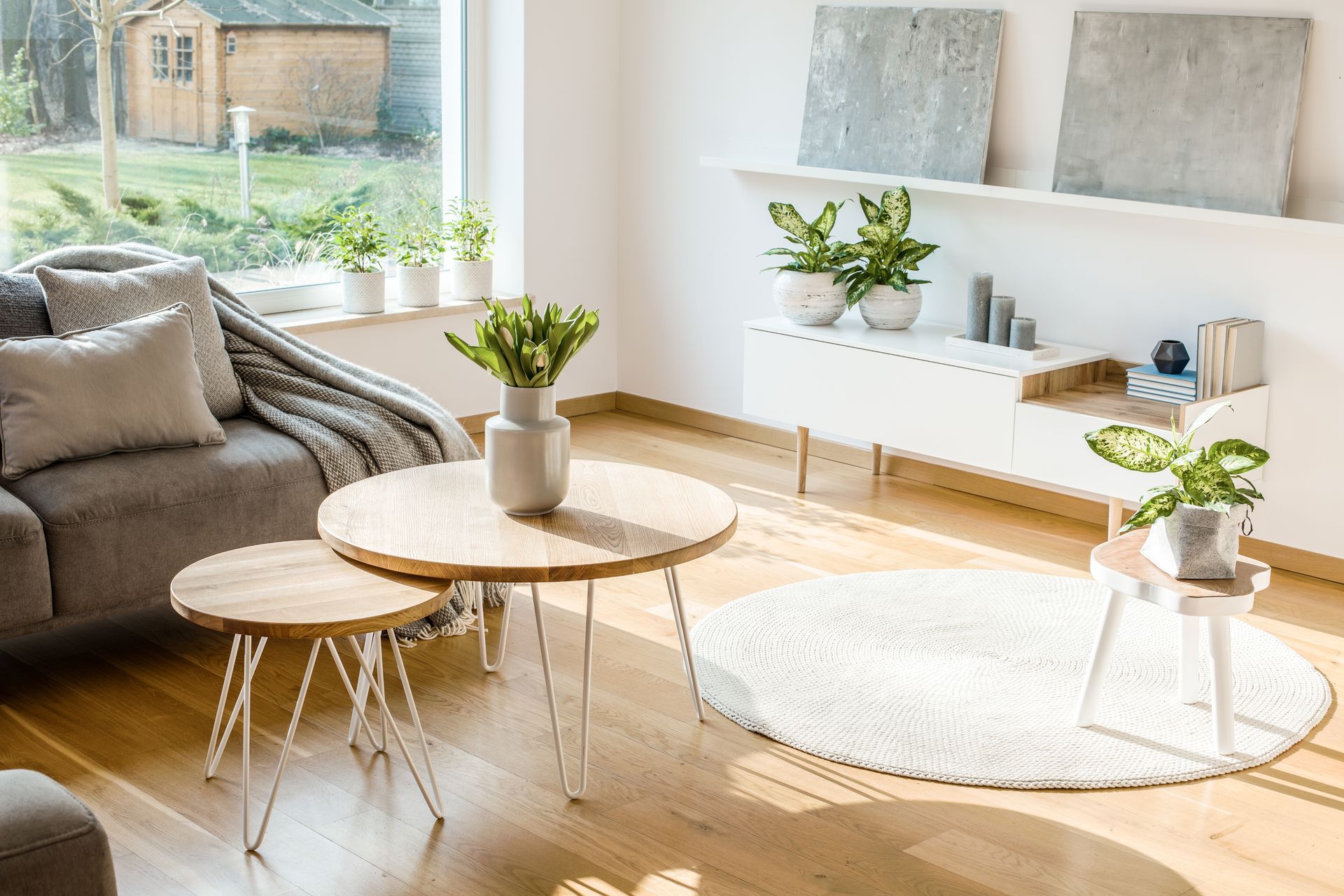 Bright living room with beige sofa, round coffee tables, plants, and sunlight on wooden floor