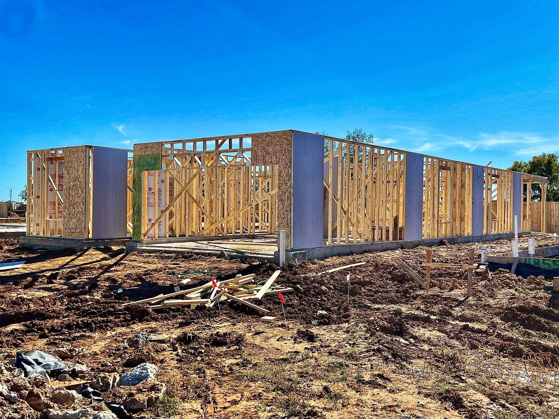 Wooden fence panels around a barren, debris-strewn lot under a bright blue sky
