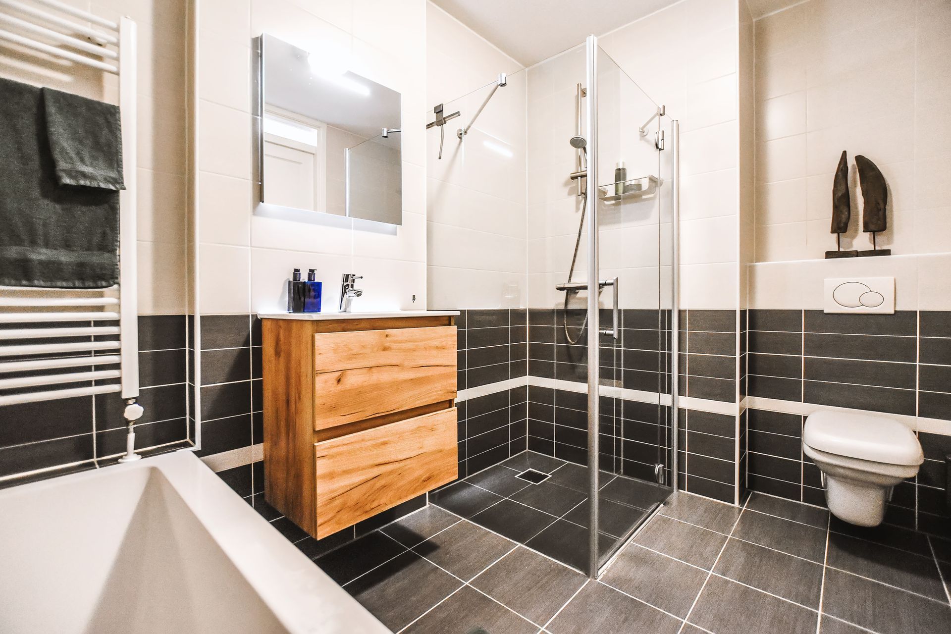 Modern bathroom with black tile, wooden vanity, glass shower, and wall-mounted toilet