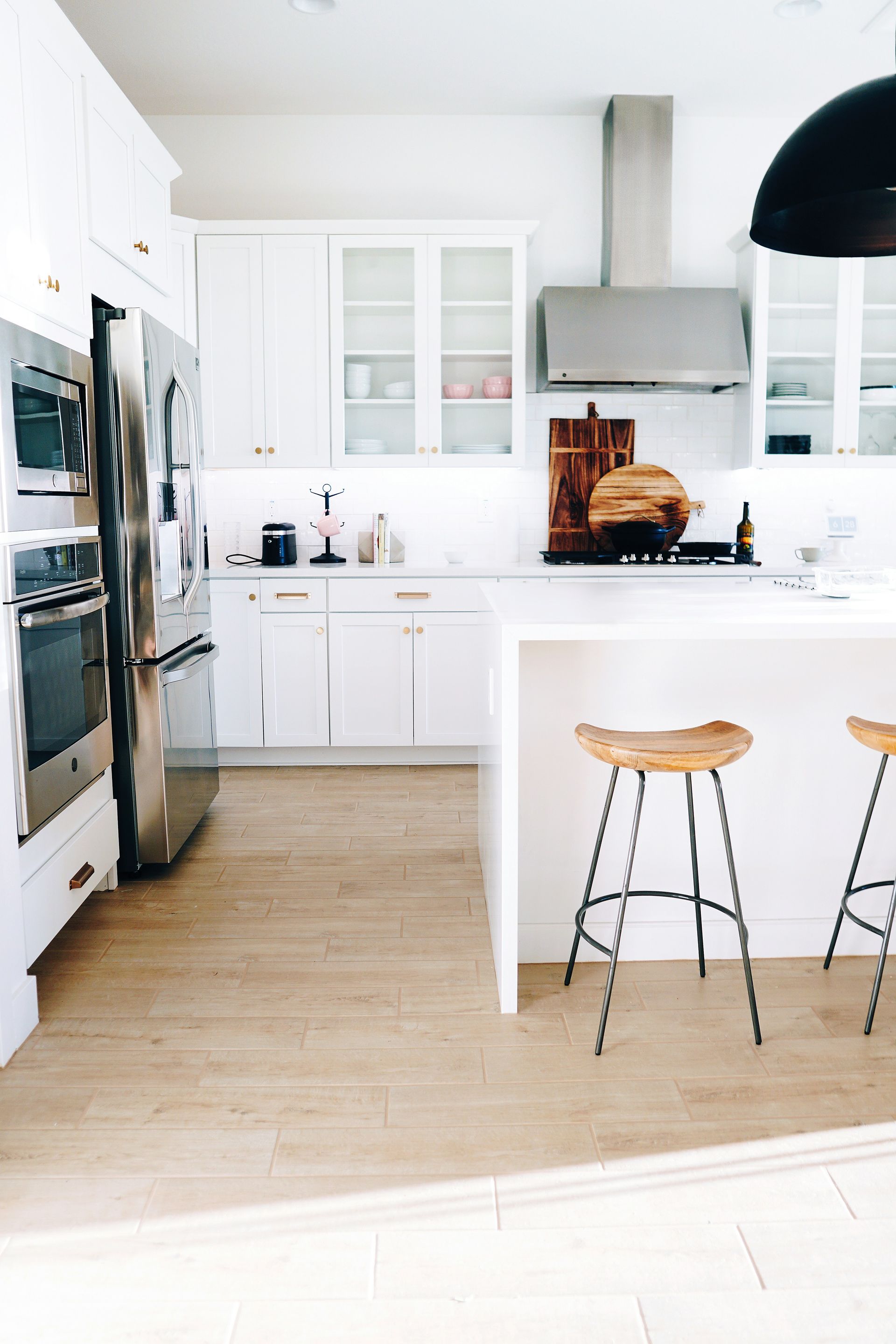 Bright white modern kitchen with stainless steel fridge, island, and two wooden bar stools