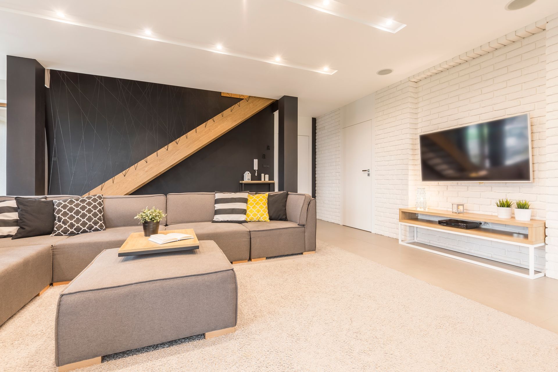 Modern living room with gray sectional sofa, wall-mounted TV, and black accent wall with diagonal wood detail