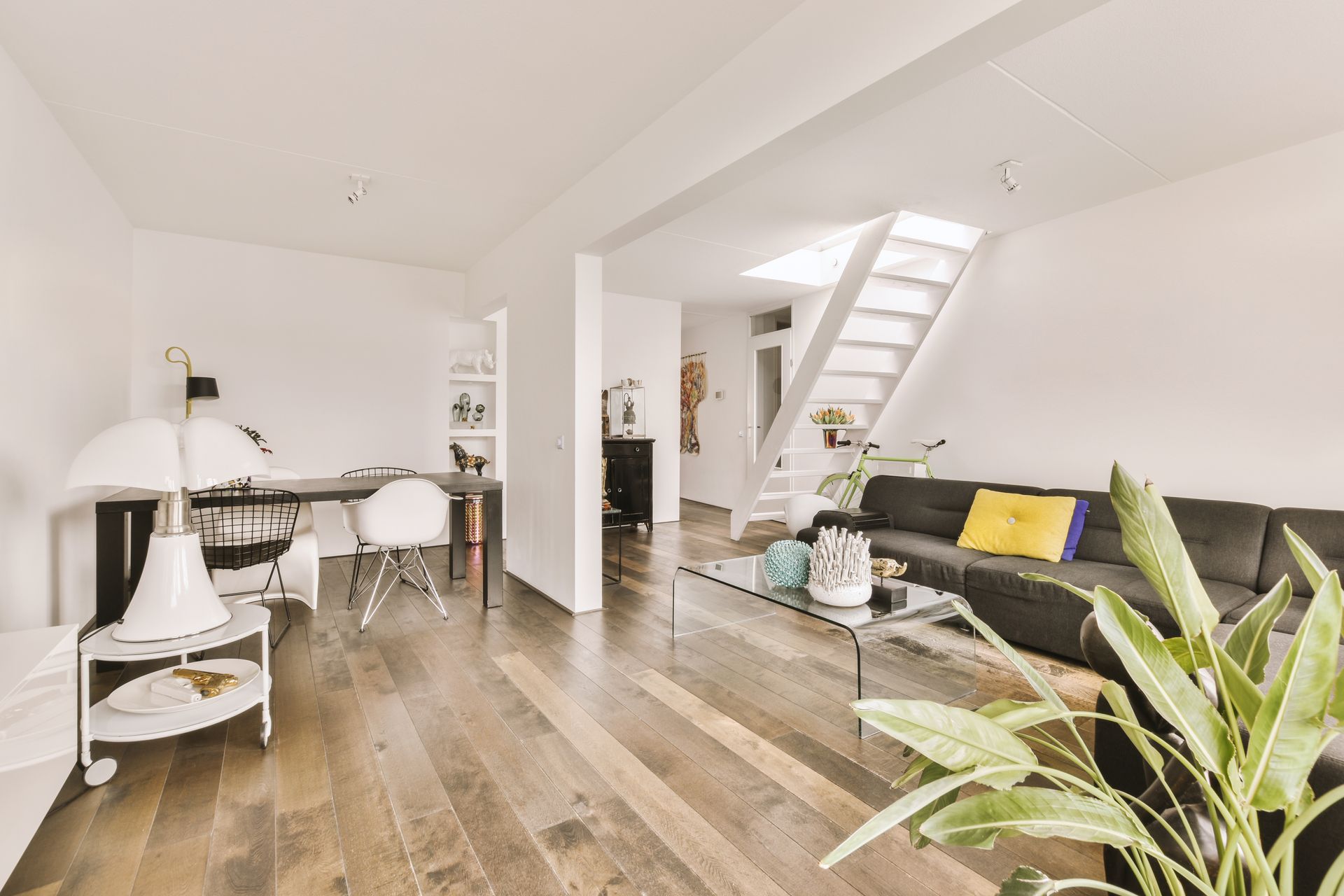 Bright modern open-plan living room with sofa, dining table, stairs, and hardwood floors