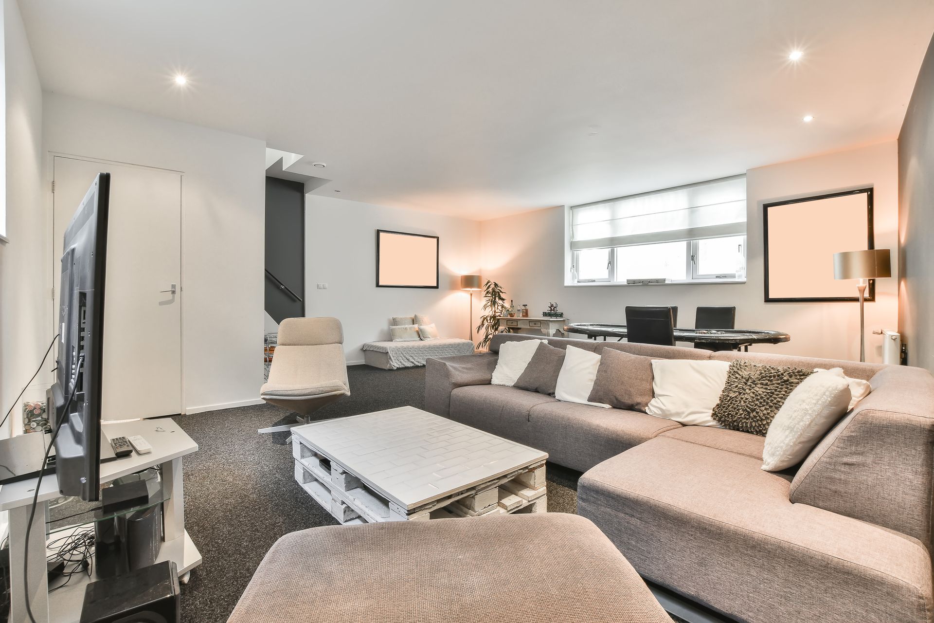 Bright modern living room with gray sectional sofa, ottoman, TV, and large windows