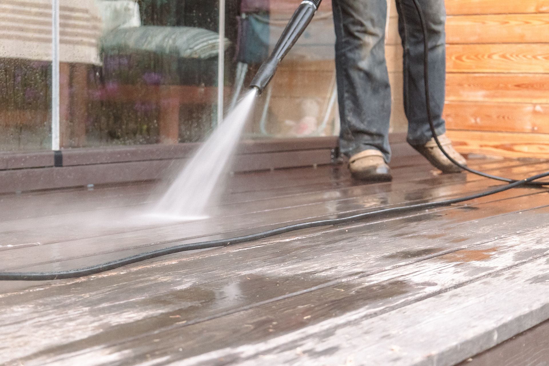 Pressure washer cleaning a wooden deck, with water spraying across the wet surface.