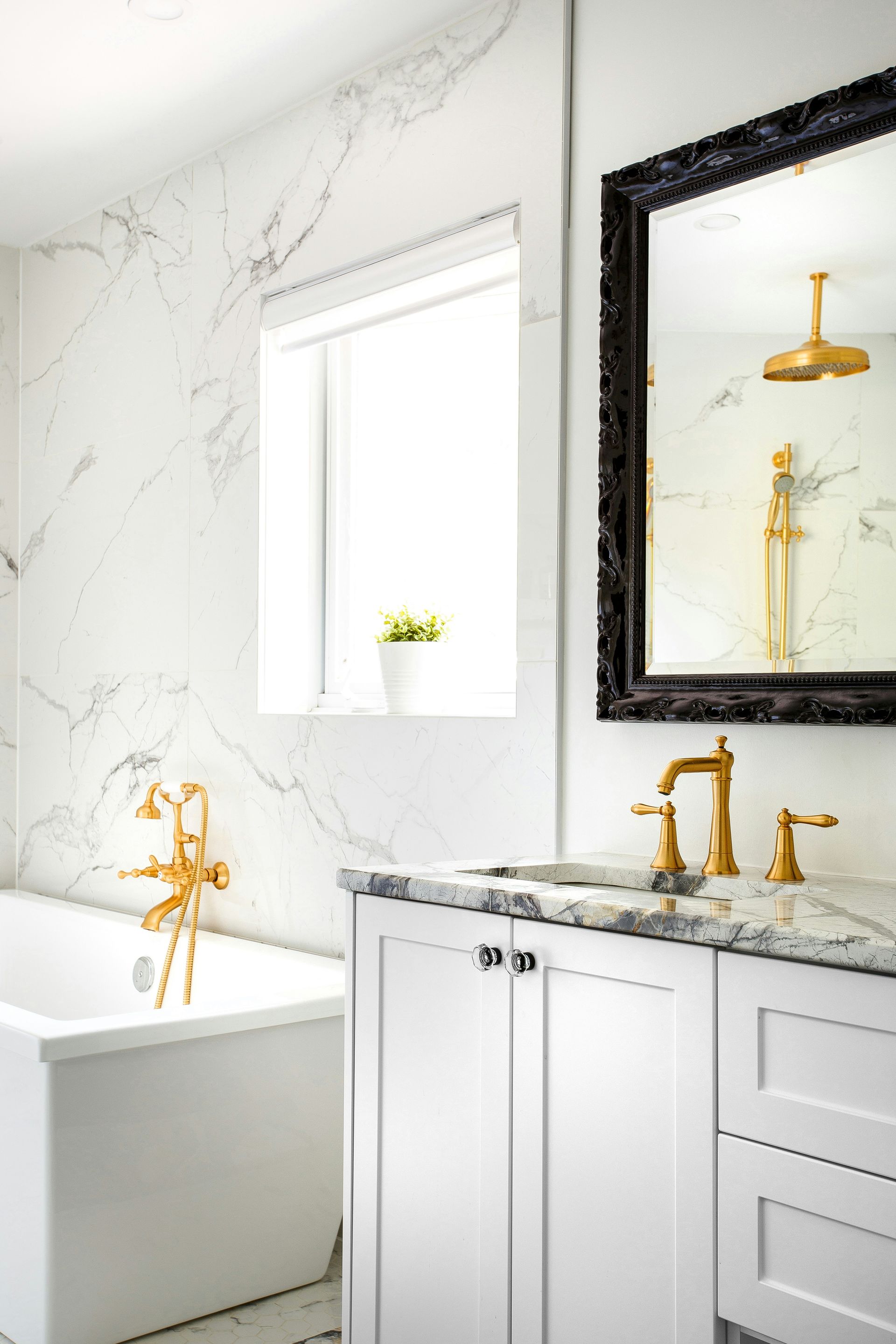Elegant white bathroom with marble walls, gold fixtures, bathtub, vanity, and mirror