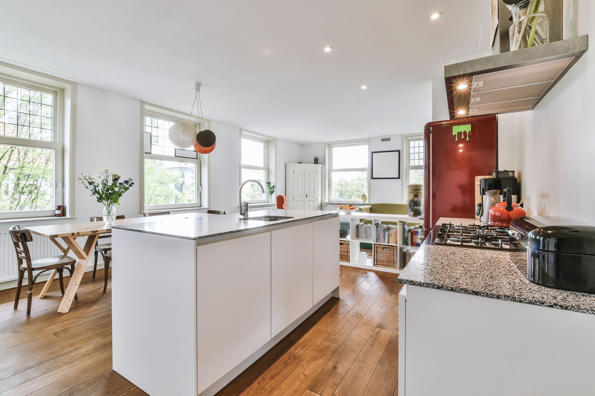 Bright modern kitchen with white island, wood floors, dining table, and red coffee machine