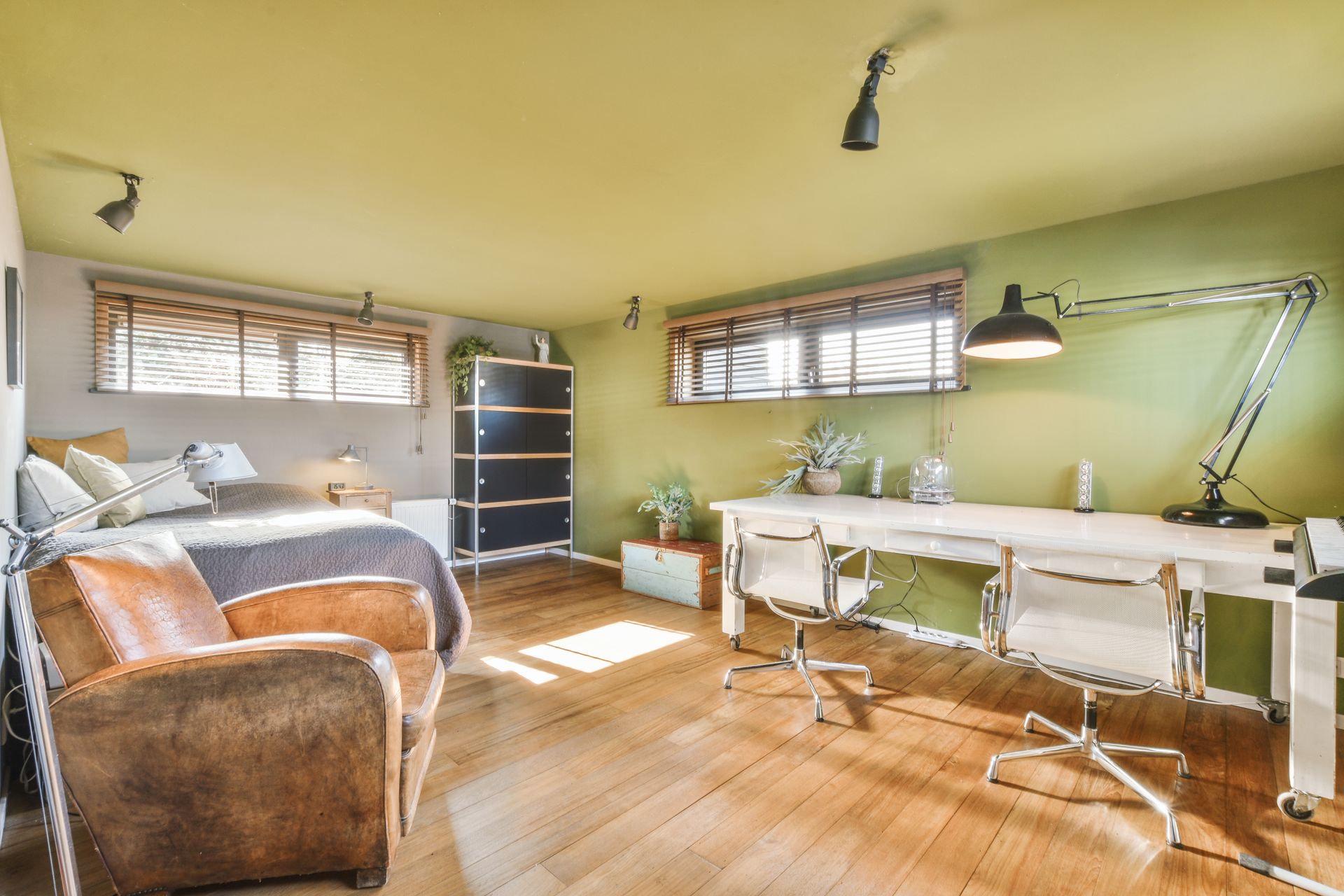 Bright home office with twin desks, swivel chair, wicker chair, shelves, and sunlight on wooden floor.