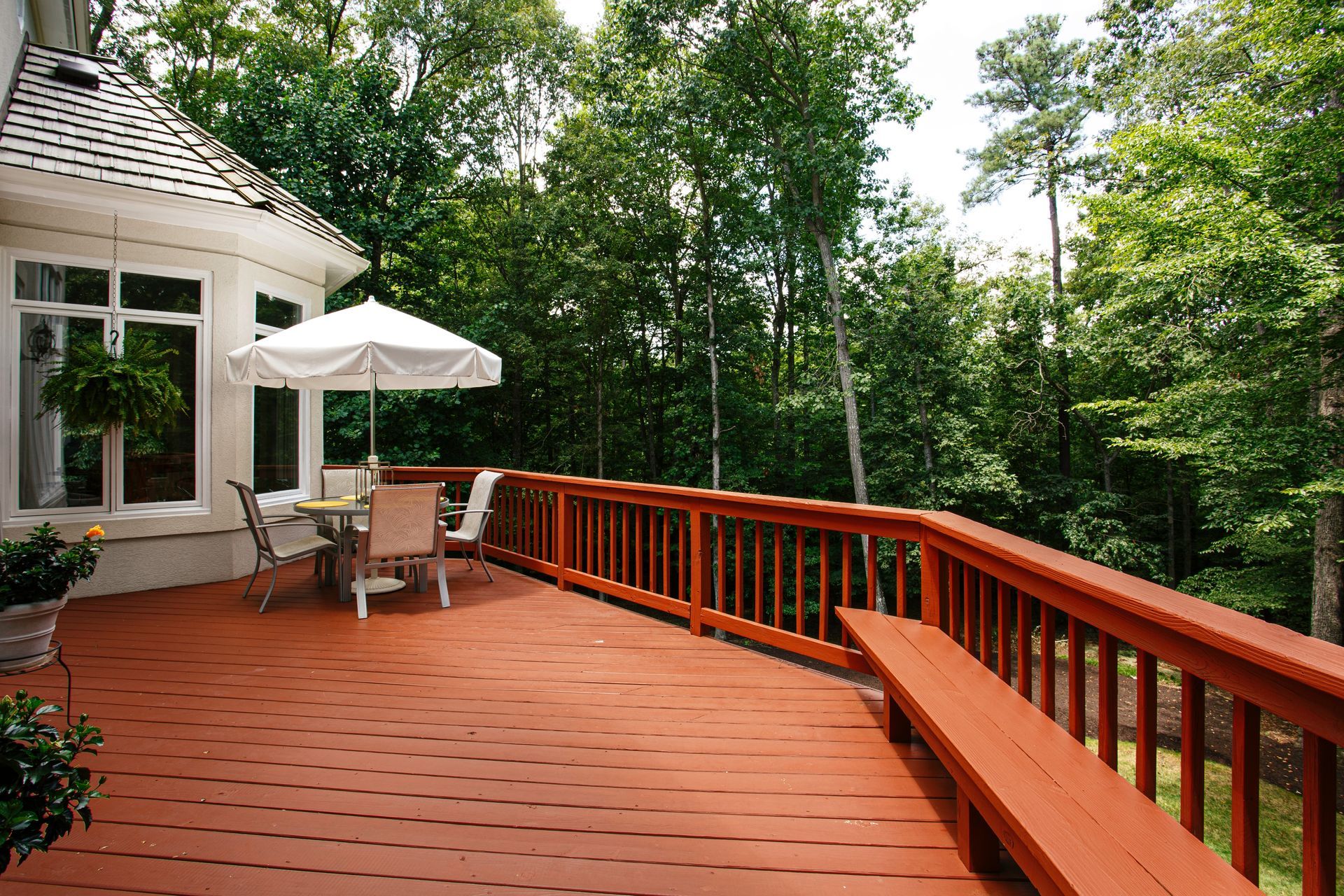 Wooden deck with patio table and white umbrella beside a house, overlooking trees