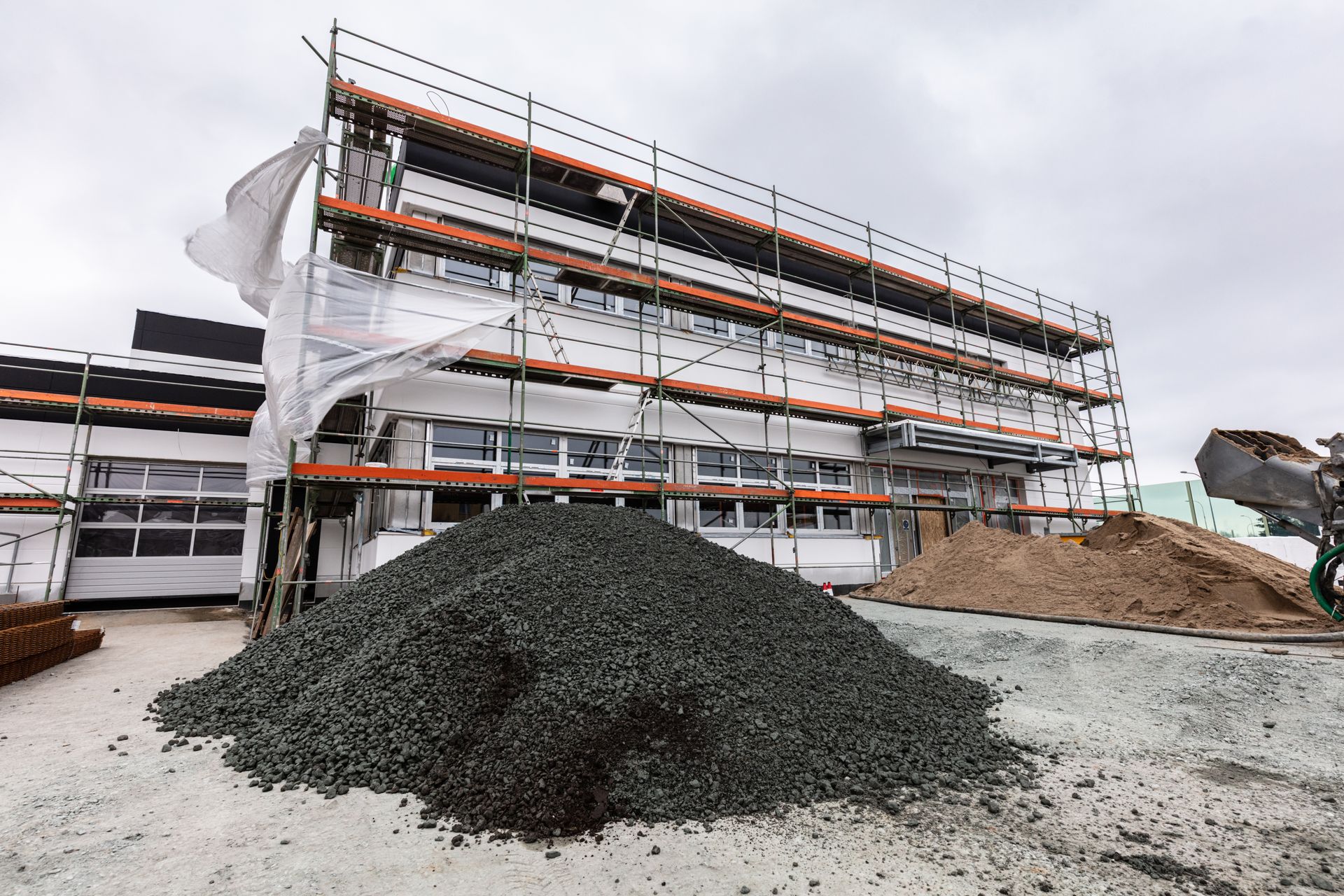 Construction site with wrapped building scaffold, dirt piles, and gravel in the foreground