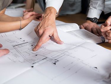 A Group of People Are Sitting Around a Table Looking at a Blueprint