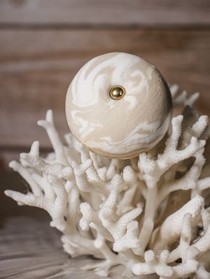 Wit, koraalachtig ornament met een crèmekleurige marmeren bol en gouden accenten op een houten ondergrond.