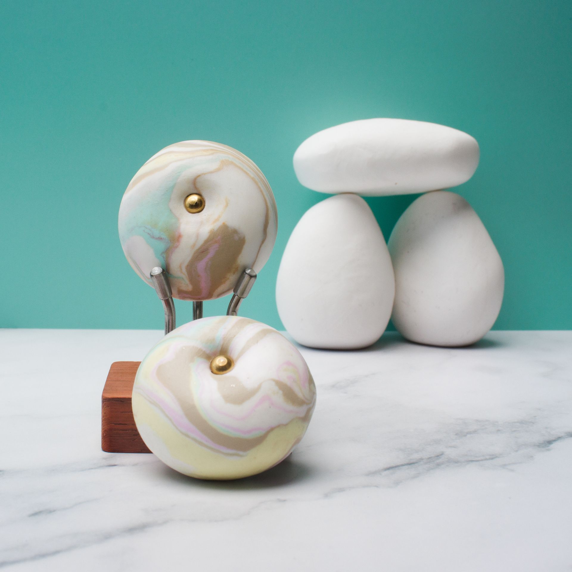 Abstracte, witte, marmerachtige bollen en gestapelde stenen op een tafelblad tegen een turquoise achtergrond.