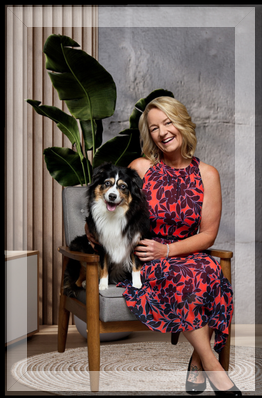 Debbie Taylor, smiling in a red and navy dress, sits with her Miniature Aussiedoodle in a modern North Idaho setting. Real estate branding for Taylor Connections is displayed beside her, featuring her tagline “Connections That Move You.”