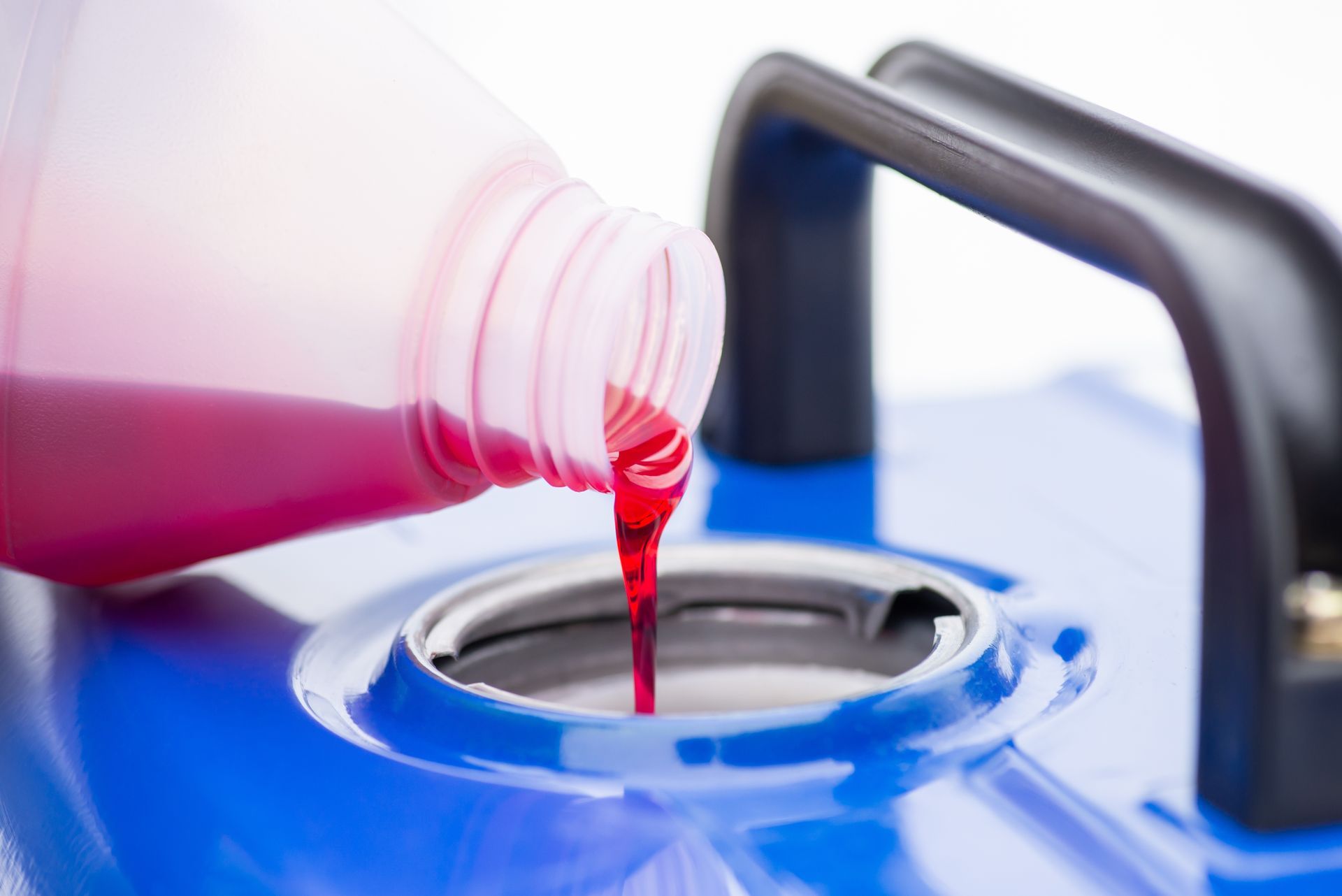 A bottle of red liquid is being poured into a blue tank.