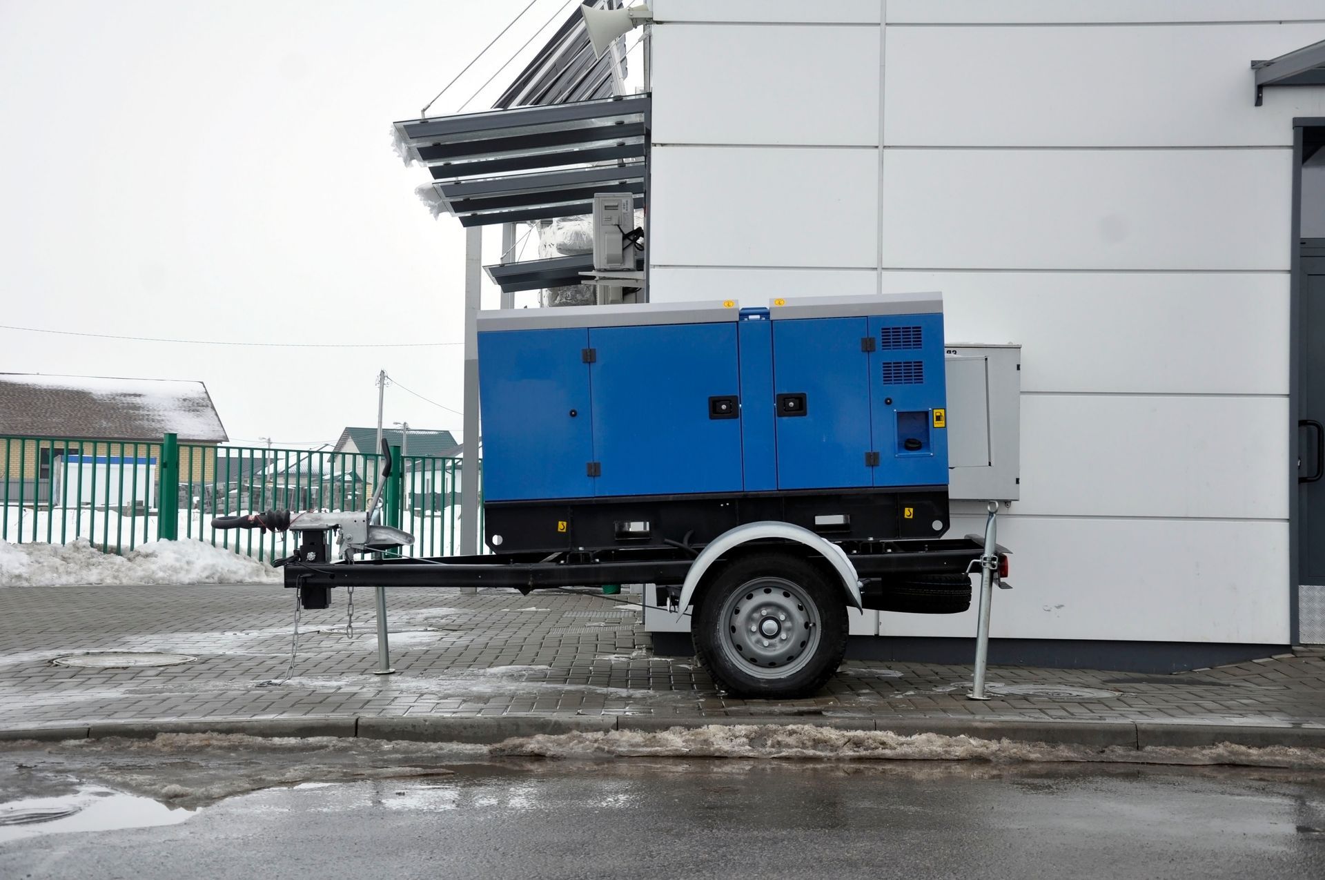 A blue generator on a trailer is parked in front of a building.