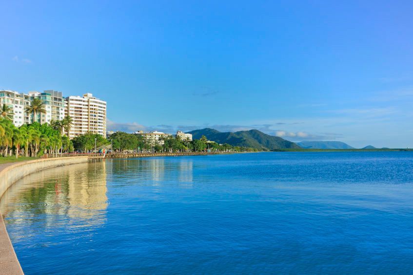 Coastal city skyline beside a calm blue bay with mountains in the distance