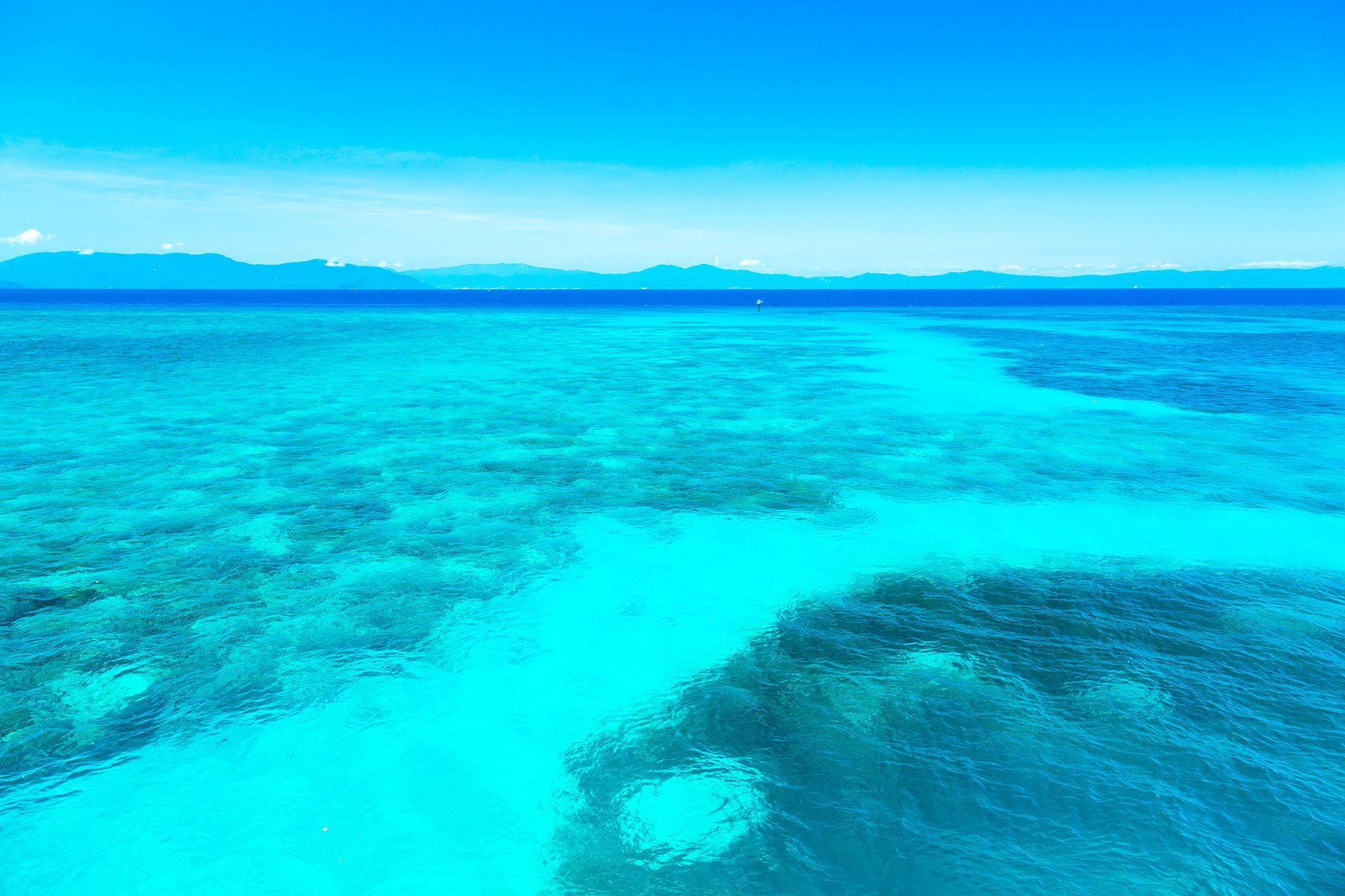 Bright turquoise ocean with a shallow sandbar and distant islands under a clear blue sky