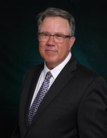 A man in a suit and tie stands in front of a dark background