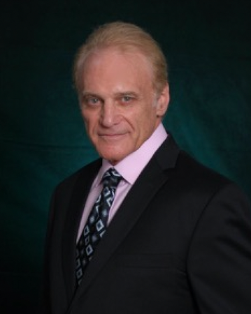 A man in a suit and tie stands in front of a green background