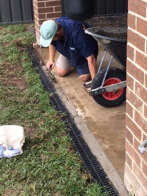 Tradesman installing a stormwater drainage grate along a brick house edge.