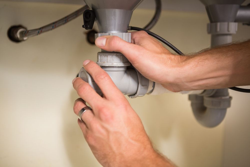 A Person is Fixing a Sink Pipe Under a Sink — Accredited Plumbing in Narrawallee, NSW