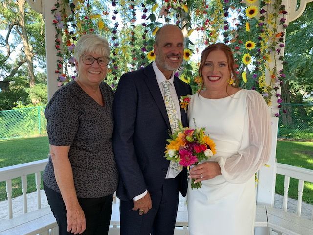 A bride and groom pose with another woman under a decorated gazebo at a wedding.