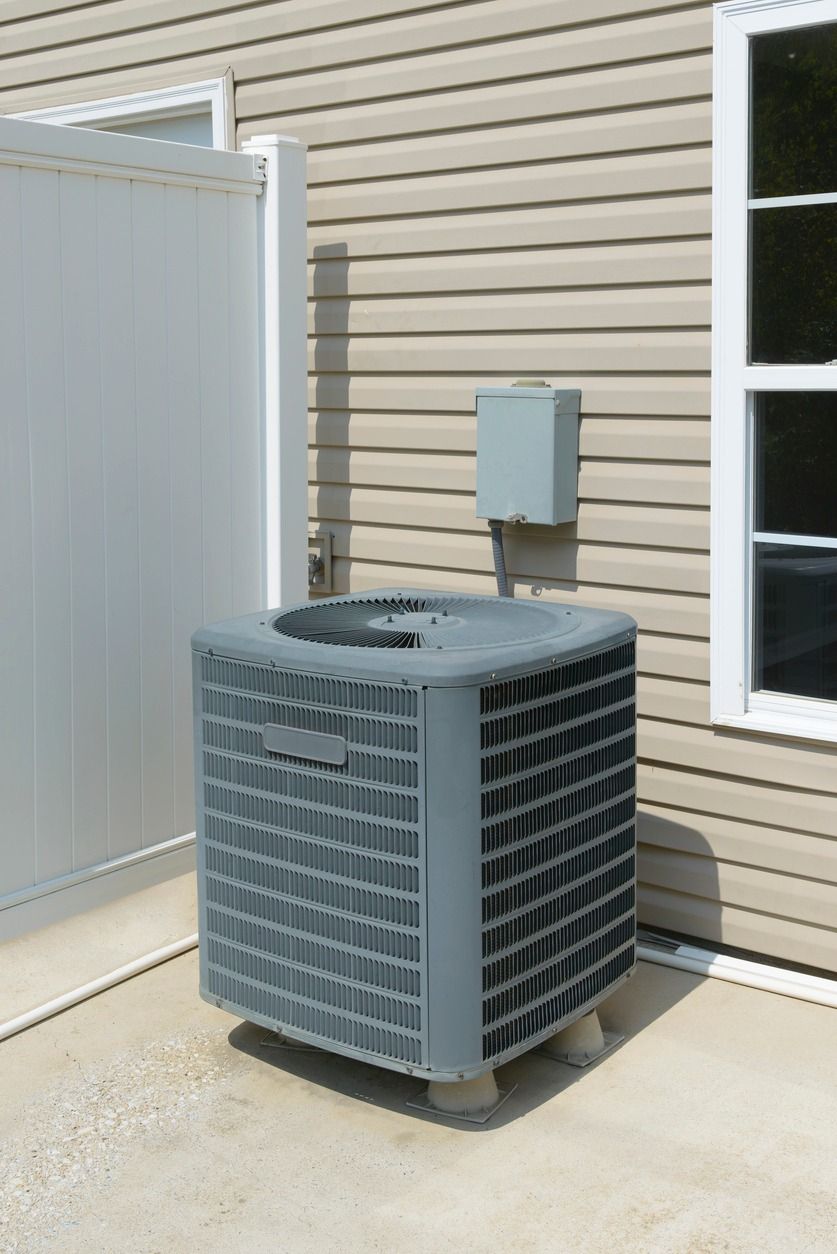 An air conditioner is sitting outside of a house next to a window.