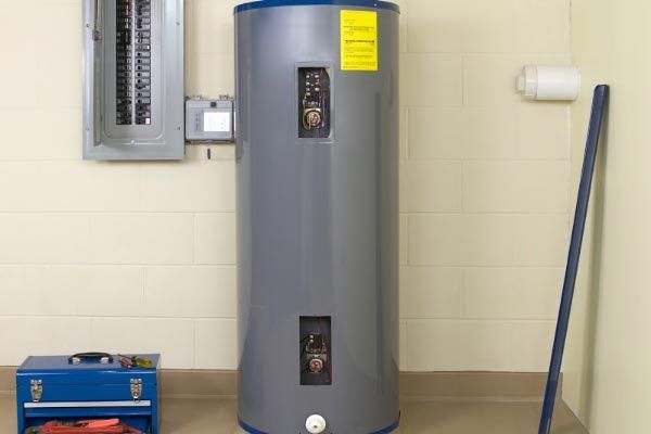 A water heater is sitting in a room next to a toolbox and mop.