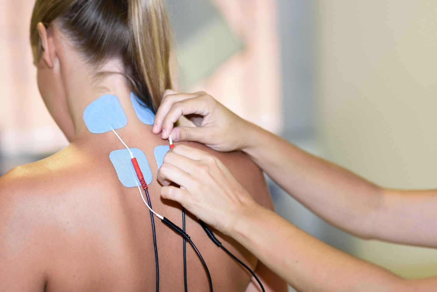 Person receiving massage therapy with electrode pads on the upper back and neck