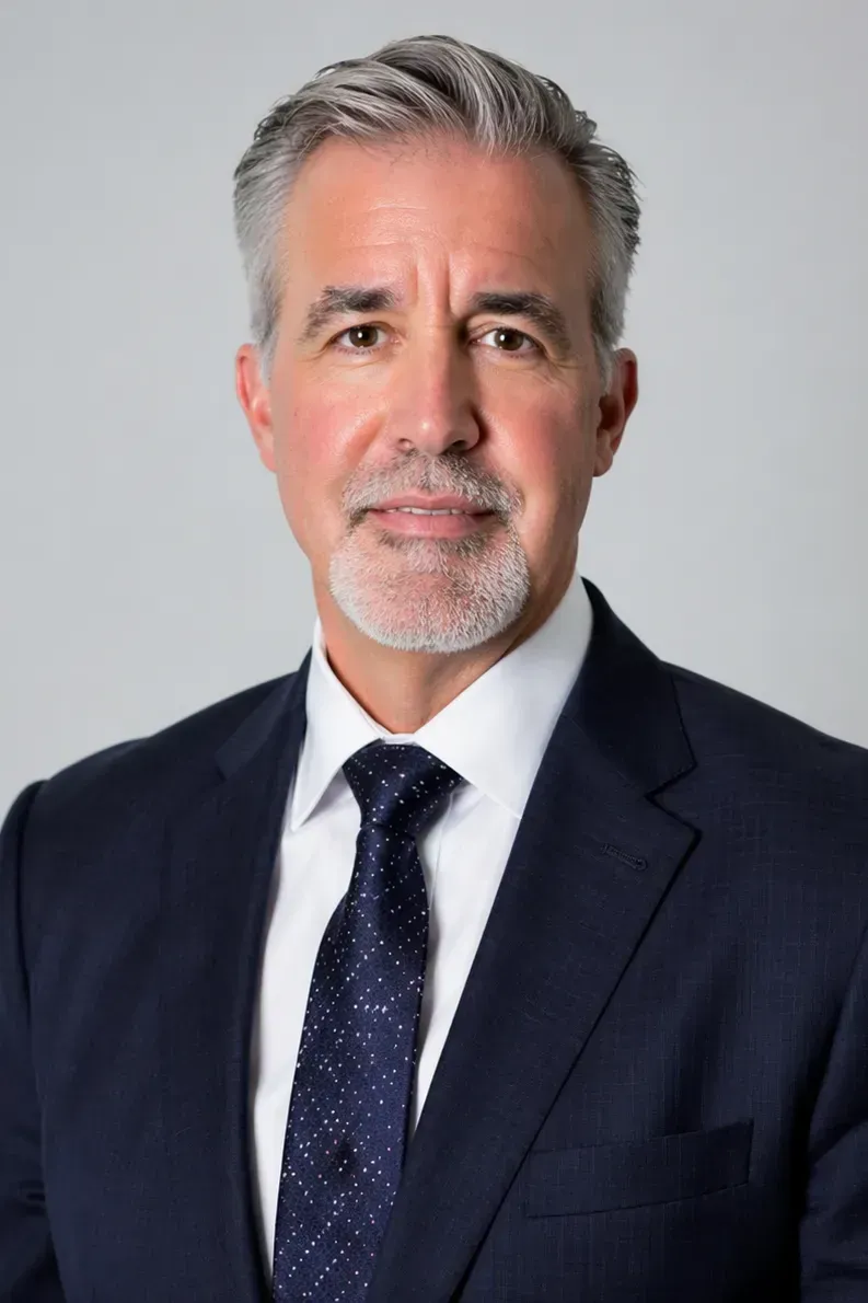 Portrait of a man in a dark suit, white shirt, and navy tie against a light gray background