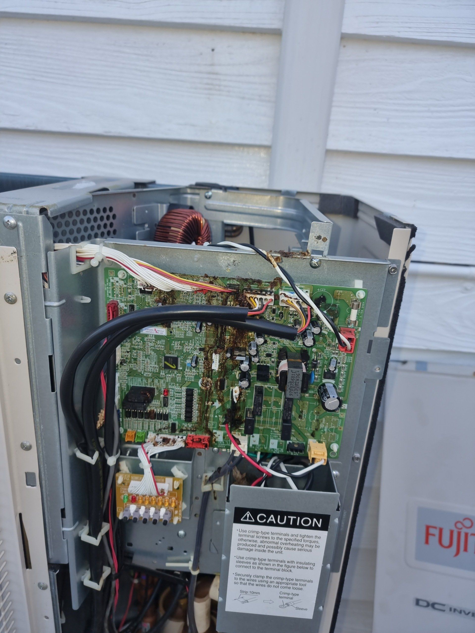 Open electrical appliance with exposed circuit boards and wiring beside a house wall
