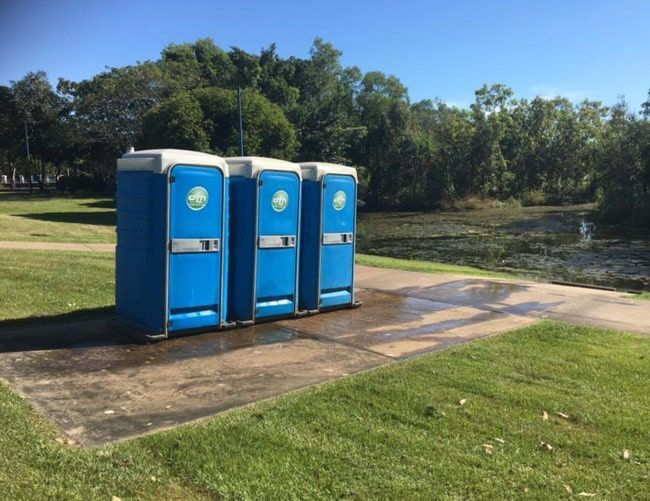 Three Blue Portable Toilets on a Concrete Pad Beside a Grassy Riverside Path — Darwin Toilet Hire in Rosebery, NT