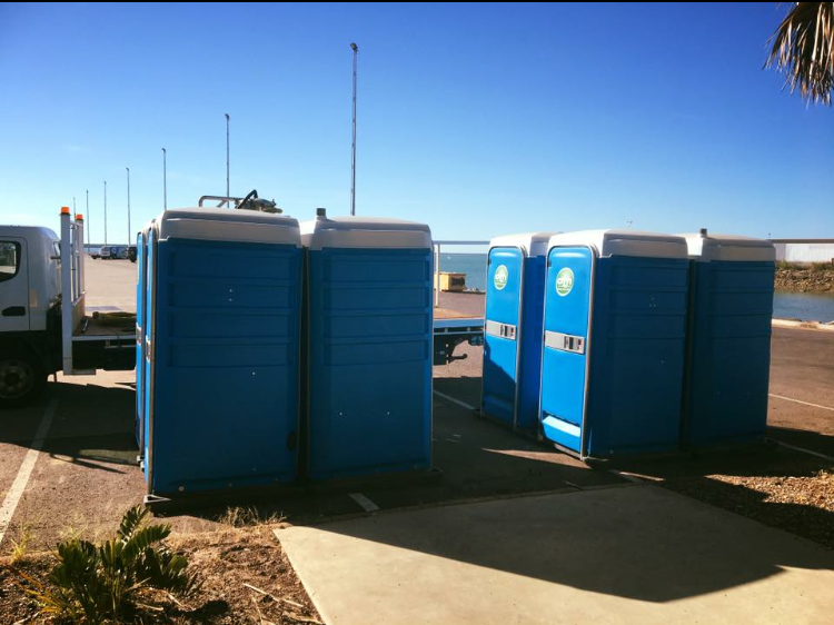 Blue Portable Toilets Lined Up Outdoors on a Sunny Beachside Area — Darwin Toilet Hire in Rosebery, NT