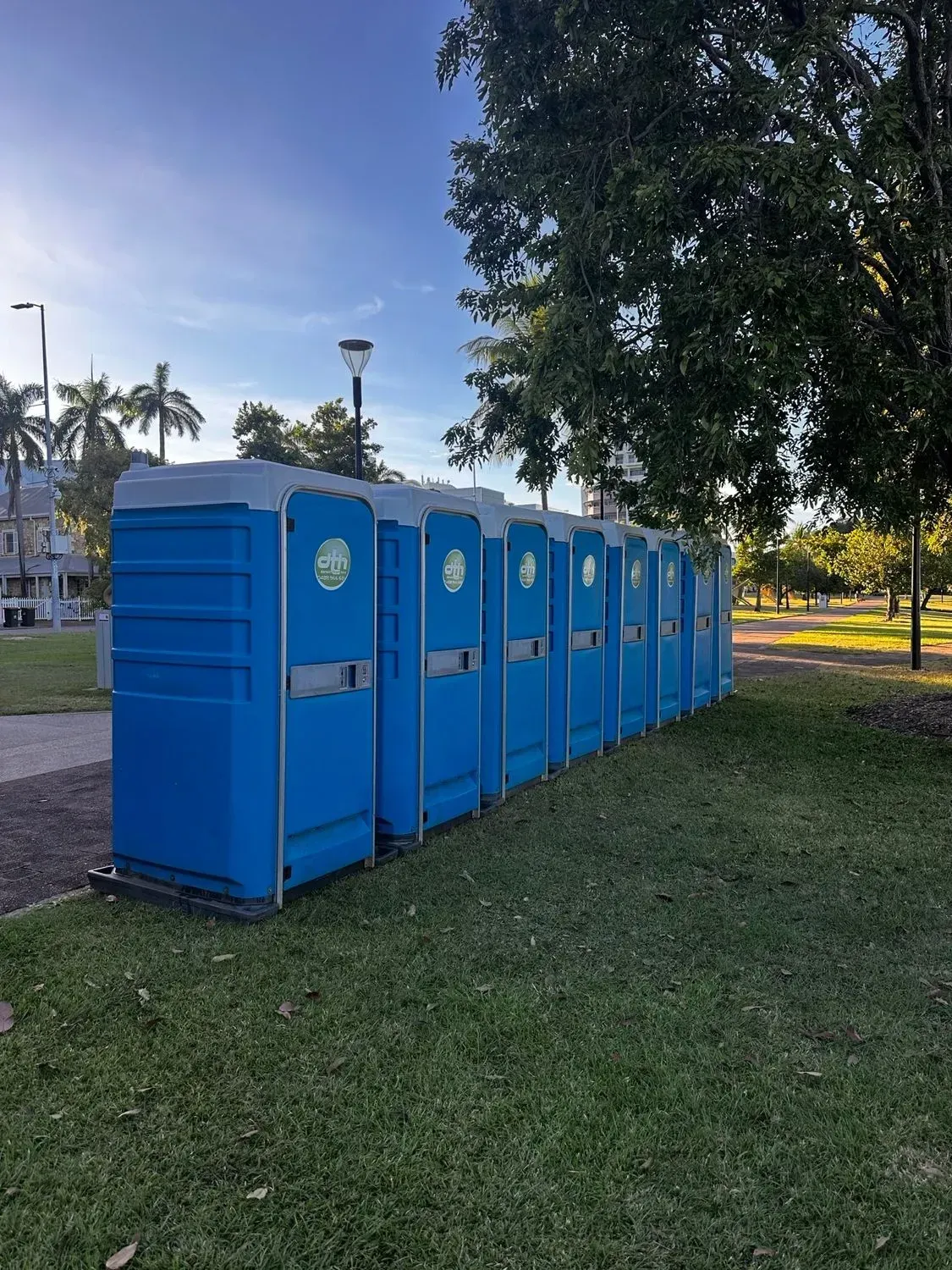 Row of Blue Portable Toilets on Grass in a Park at Sunset — Darwin Toilet Hire in Rosebery, NT