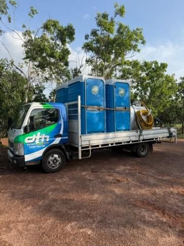 White Flatbed Truck Carrying Blue Portable Toilets on a Dirt Road With Trees — Darwin Toilet Hire in Rosebery, NT