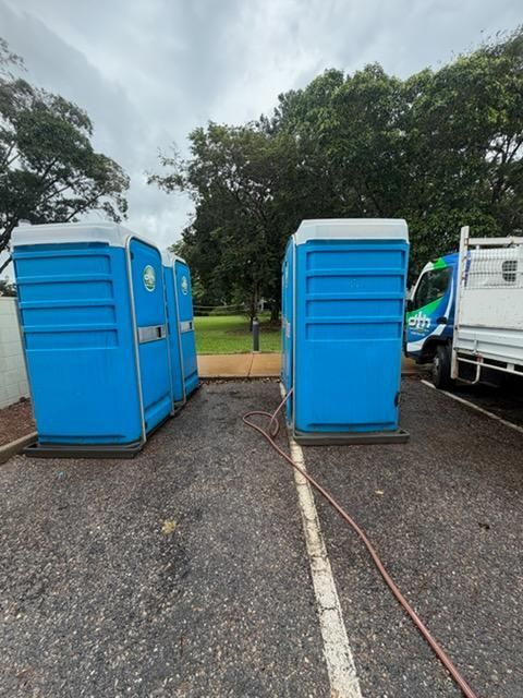 Blue Portable Toilets on Gravel at a Park, With a White Truck Beside Them — Darwin Toilet Hire in Rosebery, NT