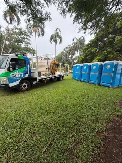 White Truck With a Flatbed Beside Blue Portable Toilets in a Grassy Park — Darwin Toilet Hire in Rosebery, NT