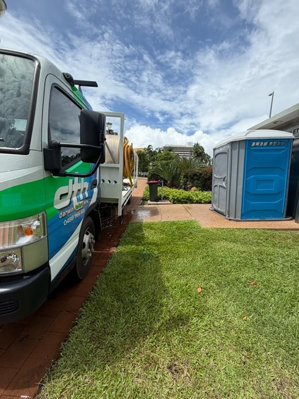 White Truck Beside Blue Portable Toilet on a Grassy Yard — Darwin Toilet Hire in Palmerston, NT