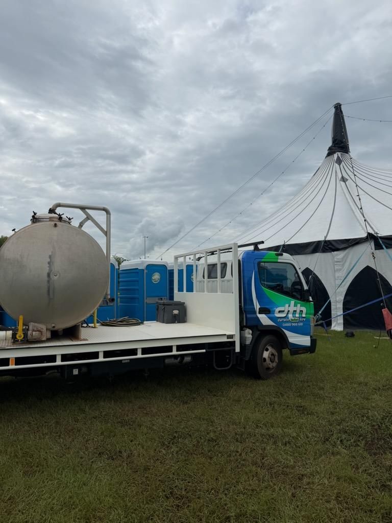 White Flatbed Truck With a Large Tank Parked on Wet Grass Beside a Blue Event Tent — Darwin Toilet Hire in Rosebery, NT