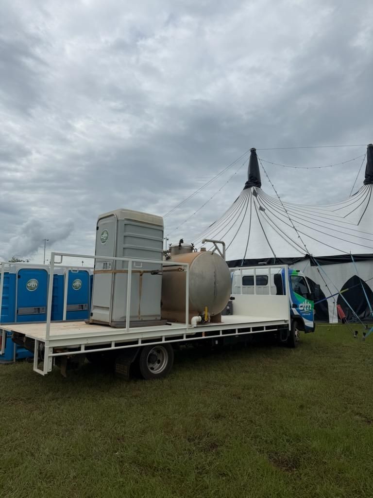 Trailer Loaded With Equipment Beside a White Tent on a Grassy Field Under a Cloudy Sky — Darwin Toilet Hire in Rosebery, NT