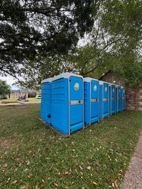 Row of Bright Blue Portable Toilets Beside a Brick Wall — Darwin Toilet Hire in Rosebery, NT